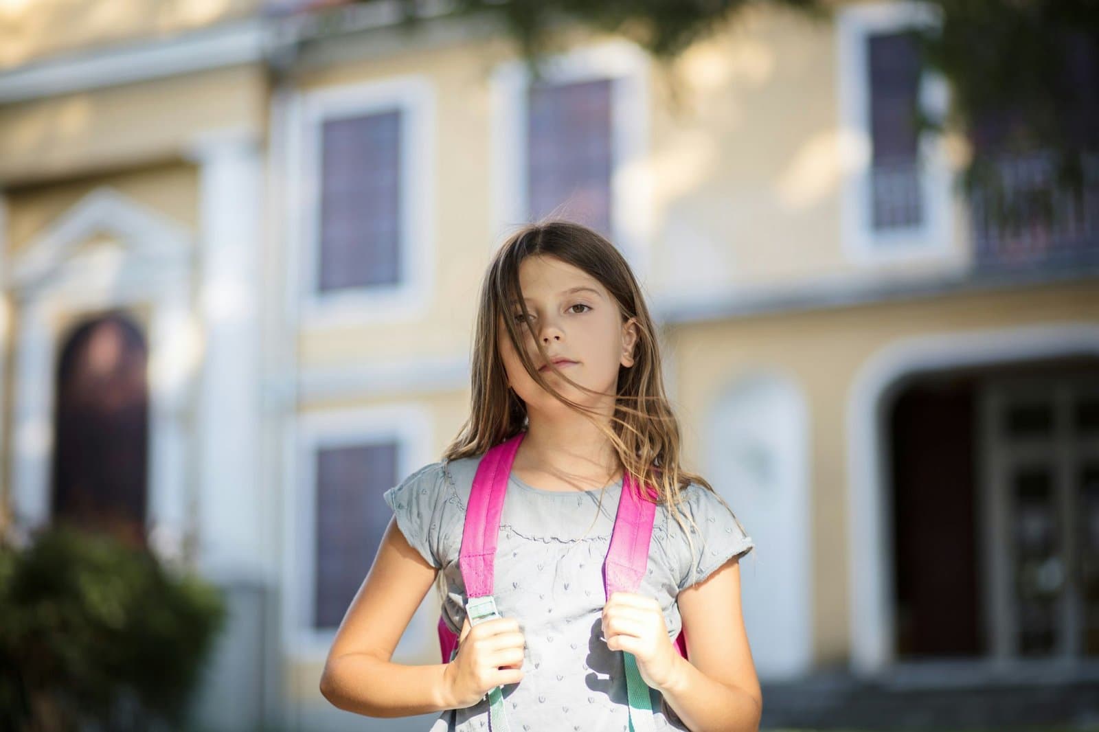 Retrato em plano médio de uma garota ao ar livre em frente a uma escola.