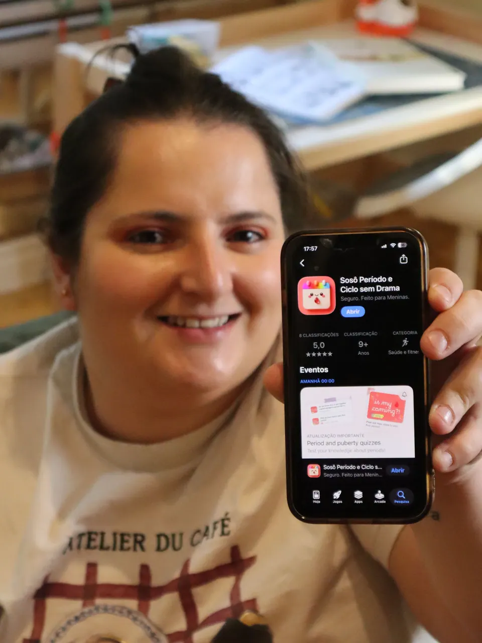Verônica smiling and holding up a phone with the Soso app on the App Store